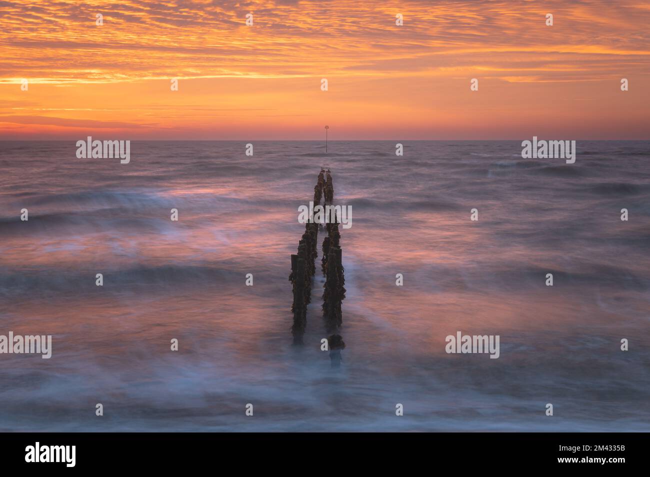Lever de soleil sur la mer du Nord sur l'île de Mersea est dans l'Essex. Wavebreaker dans la mer longue exposition. Ciel chaud, rouge, orange et jaune le matin. Couleurs éclatantes Banque D'Images