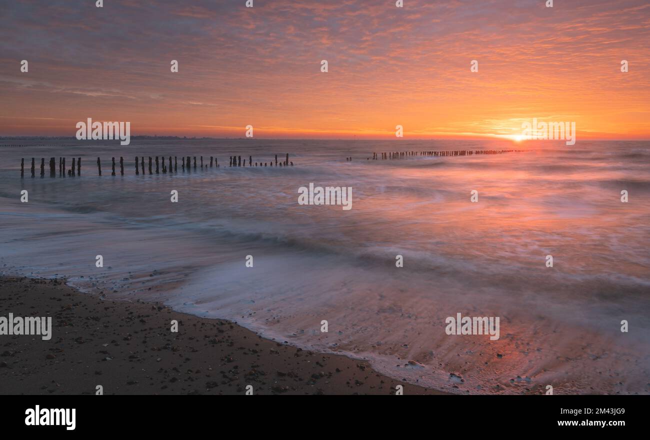Lever de soleil sur la mer du Nord sur l'île de Mersea est dans l'Essex. Wavebreaker dans la mer longue exposition. Ciel chaud, rouge, orange et jaune le matin. Couleurs éclatantes Banque D'Images
