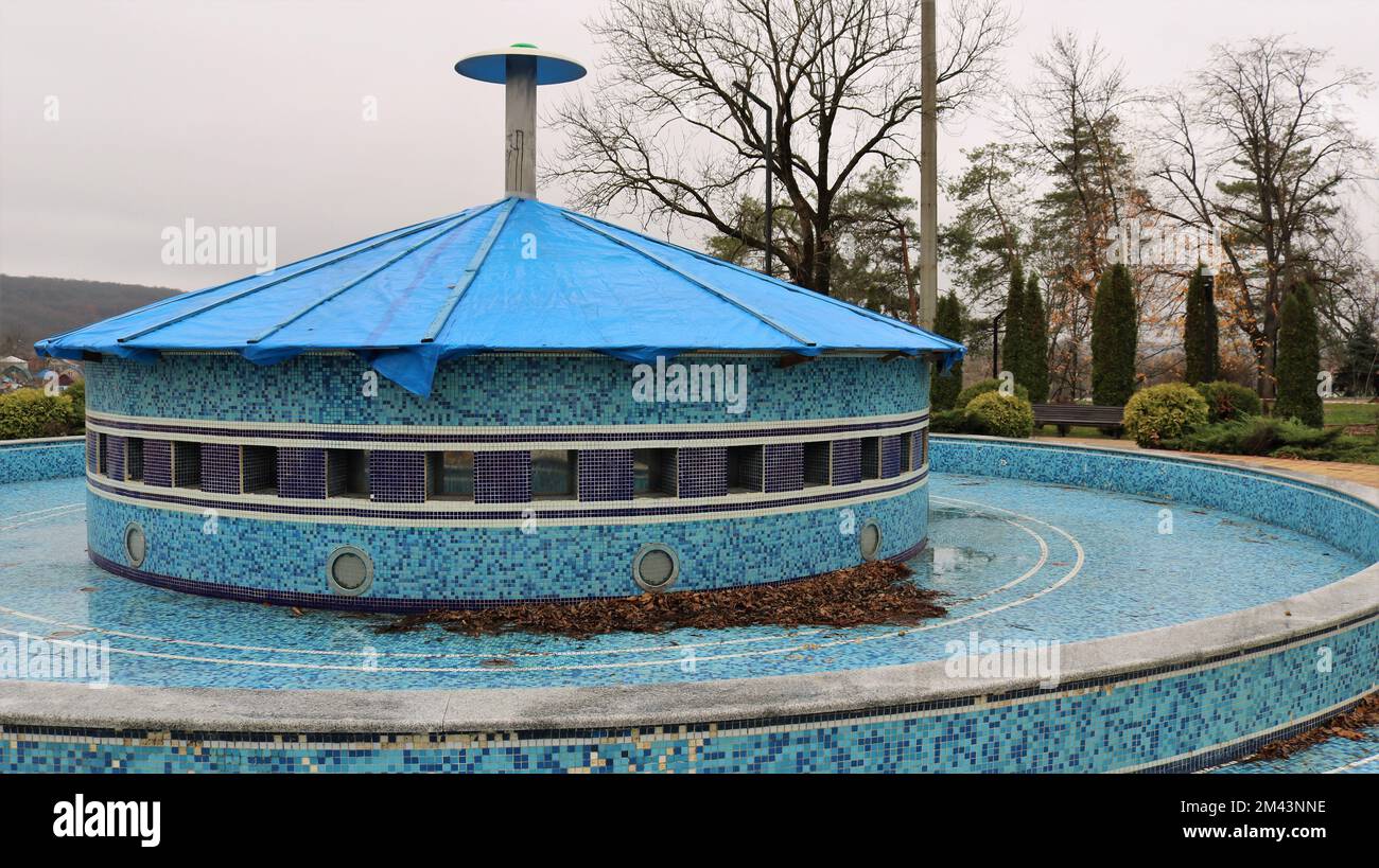 fontaine de ville inactive décorée de petites mosaïques bleues couvertes d'un auvent et couvertes de feuilles mortes sèches en basse saison Banque D'Images