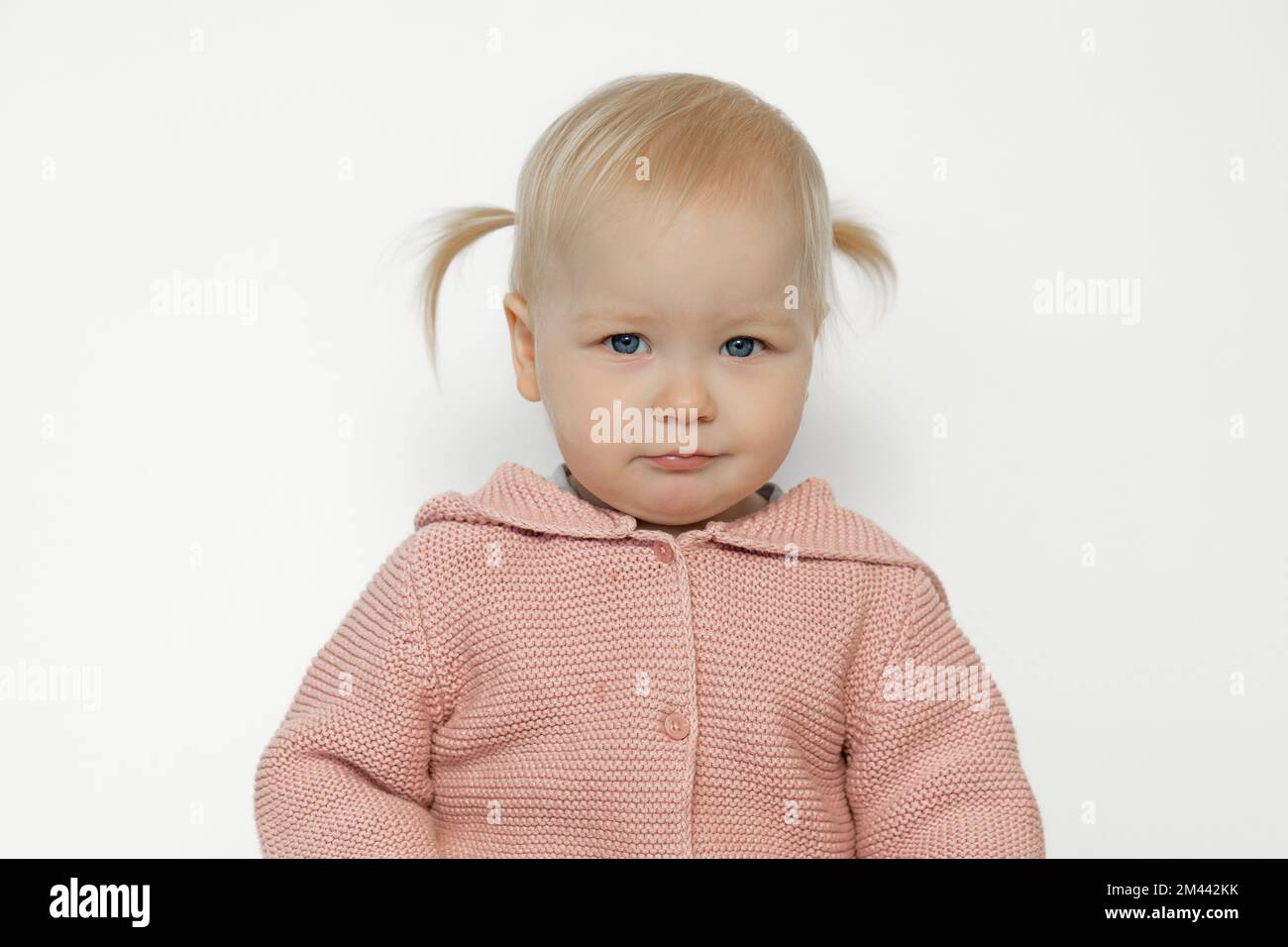 Belle fille de bébé content isolée sur blanc. Portrait d'un tout-petit amusé en studio. Enfant blond aux cheveux avec une expression du visage heureuse en tricot rose Banque D'Images