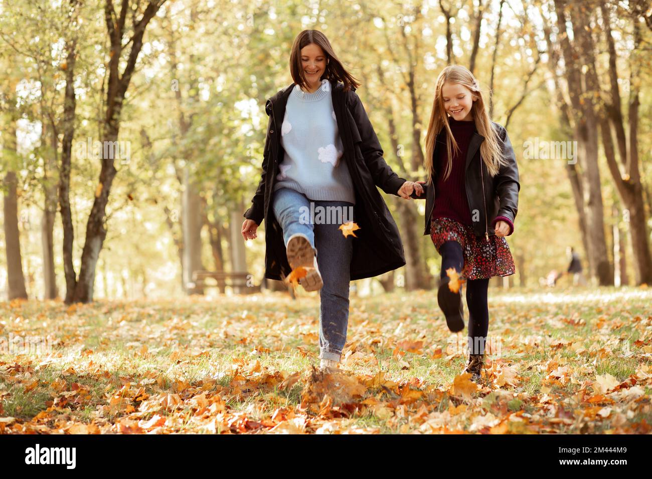 Mischier, ludique, heureux, souriante femme et fille jouent et dansent, kick feuilles dans la forêt dorée d'automne. Amuse-toi bien Banque D'Images