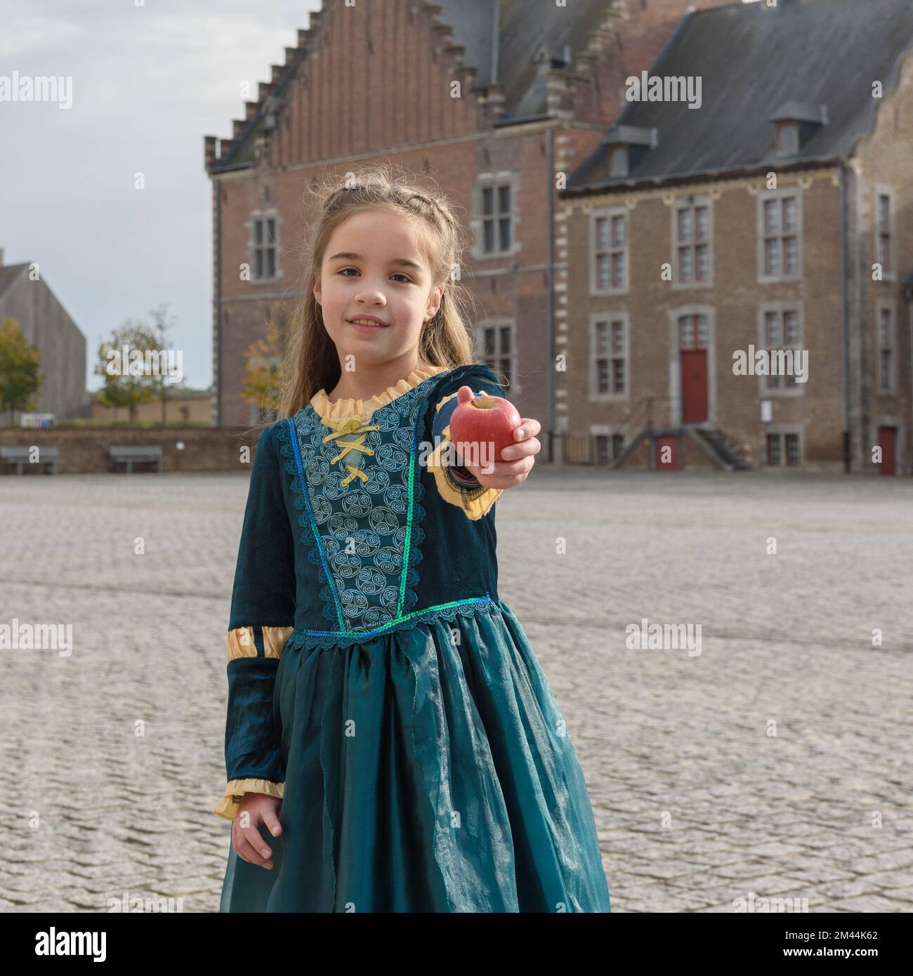 Une petite fille dans une robe médiévale contre le château s'étire une  pomme rouge. Format carré Photo Stock - Alamy