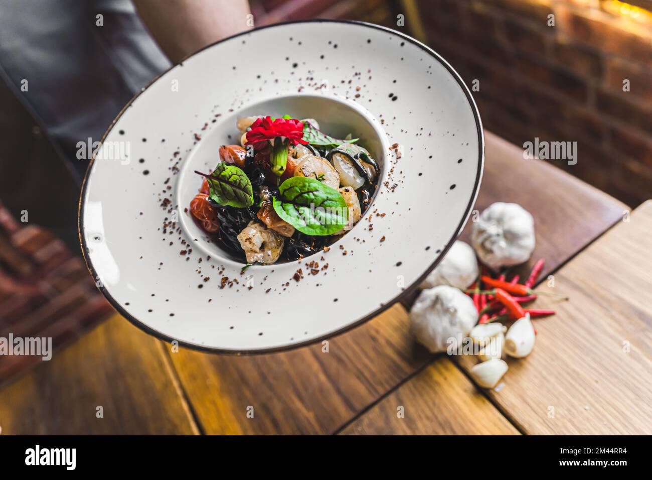 Un serveur méconnu servant des crevettes. Pâtes à base de tagliolini noires aux crevettes et aux herbes. Intérieur du restaurant. Photo de haute qualité Banque D'Images