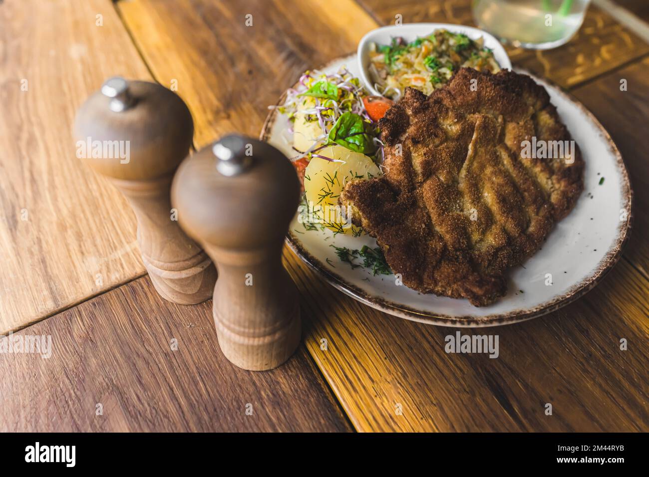 Le plat polonais du restaurant, la schabowy, sert une hache de porc avec des pommes de terre et des légumes sur une assiette blanche, ainsi qu'un saupoudreuse de poivre et de sel. Vue grand angle. Prise de vue en intérieur. Photo de haute qualité Banque D'Images