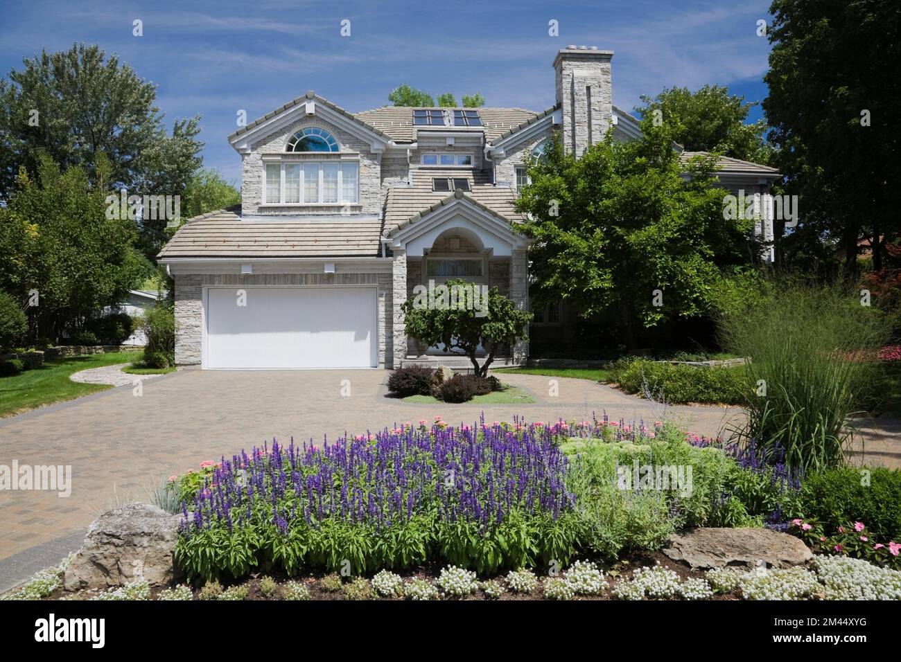 Maison contemporaine de style cottage en briques grises avec cour avant paysagée en été. Banque D'Images