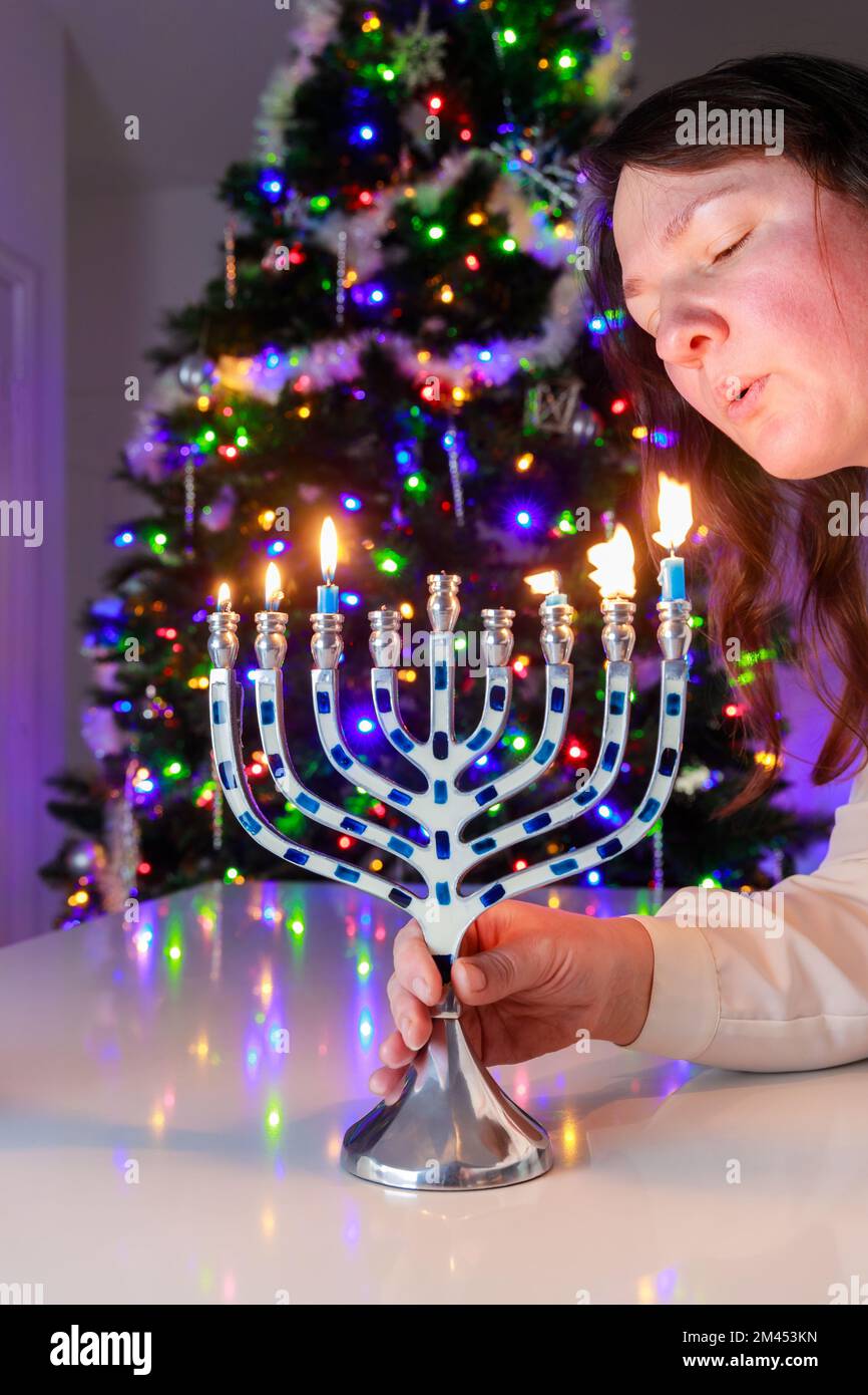 La femme juive souffle les bougies sur la menorah d'Hanoukkah avec neuf bougies. Banque D'Images