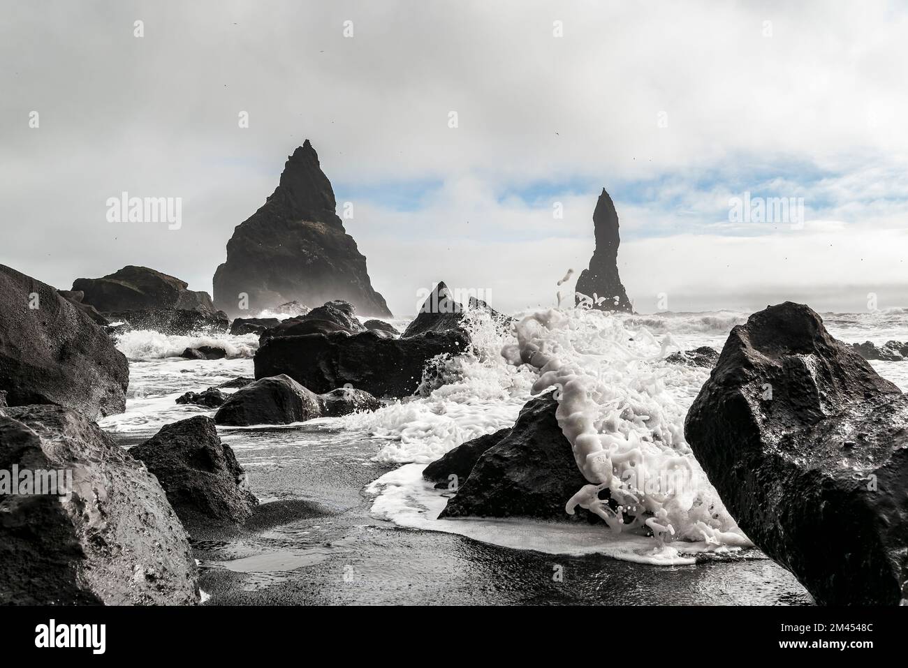 Les vagues s'écrasant contre les rochers noirs de basalte de la plage de Reynisfjara, avec les piles de la mer de Reynisdrangar en arrière-plan, près de Vík í Mýrdal, en Islande Banque D'Images