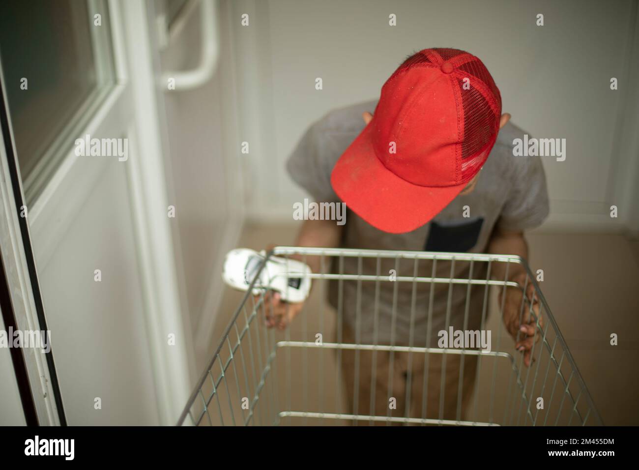 L'enfant pousse le chariot de l'épicerie dans la magie. L'enfant fait des choses stupides. Mauvais comportement de l'adolescent. Capuchon rouge sur la tête du garçon. Entrée du magasin. Banque D'Images