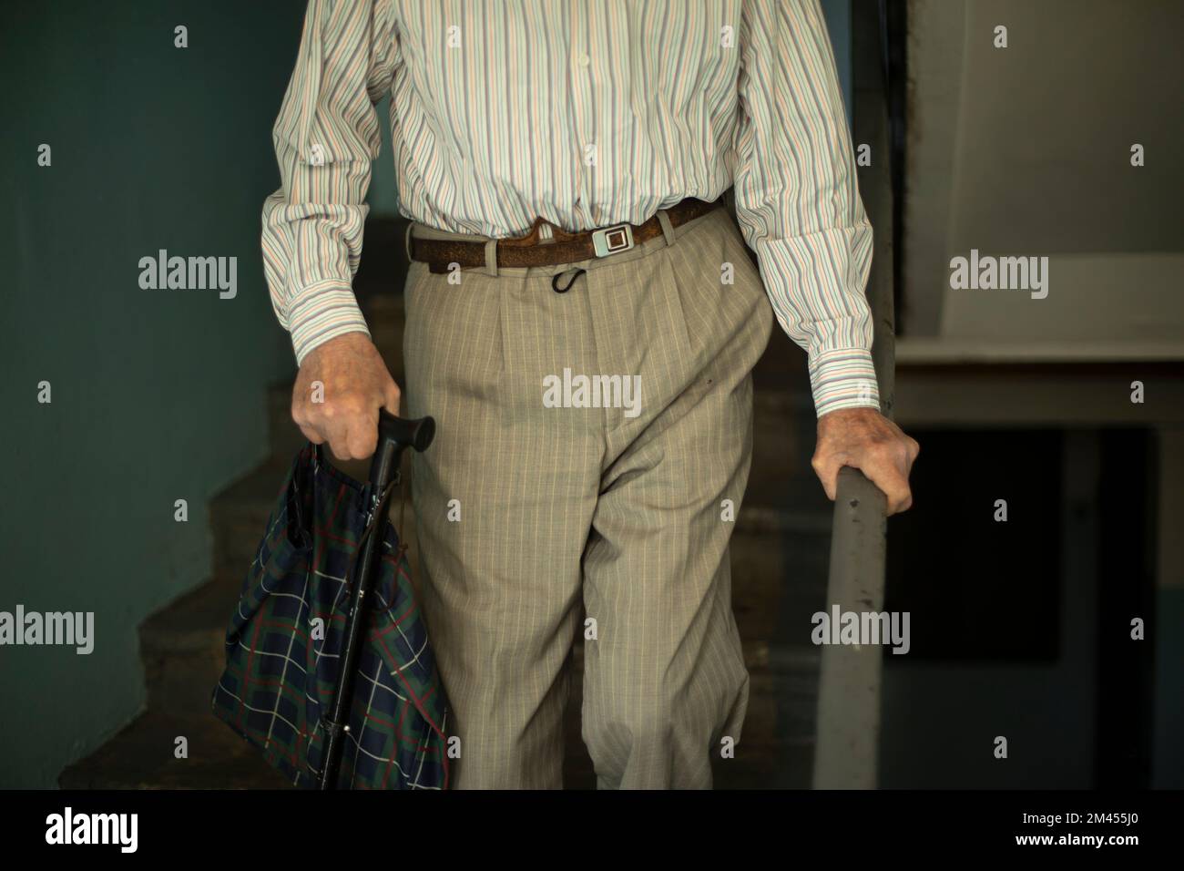 Le pensionné descend les escaliers.Grandpa descend les marches.Vieil homme en Russie.La main se tient sur la main courante. Banque D'Images