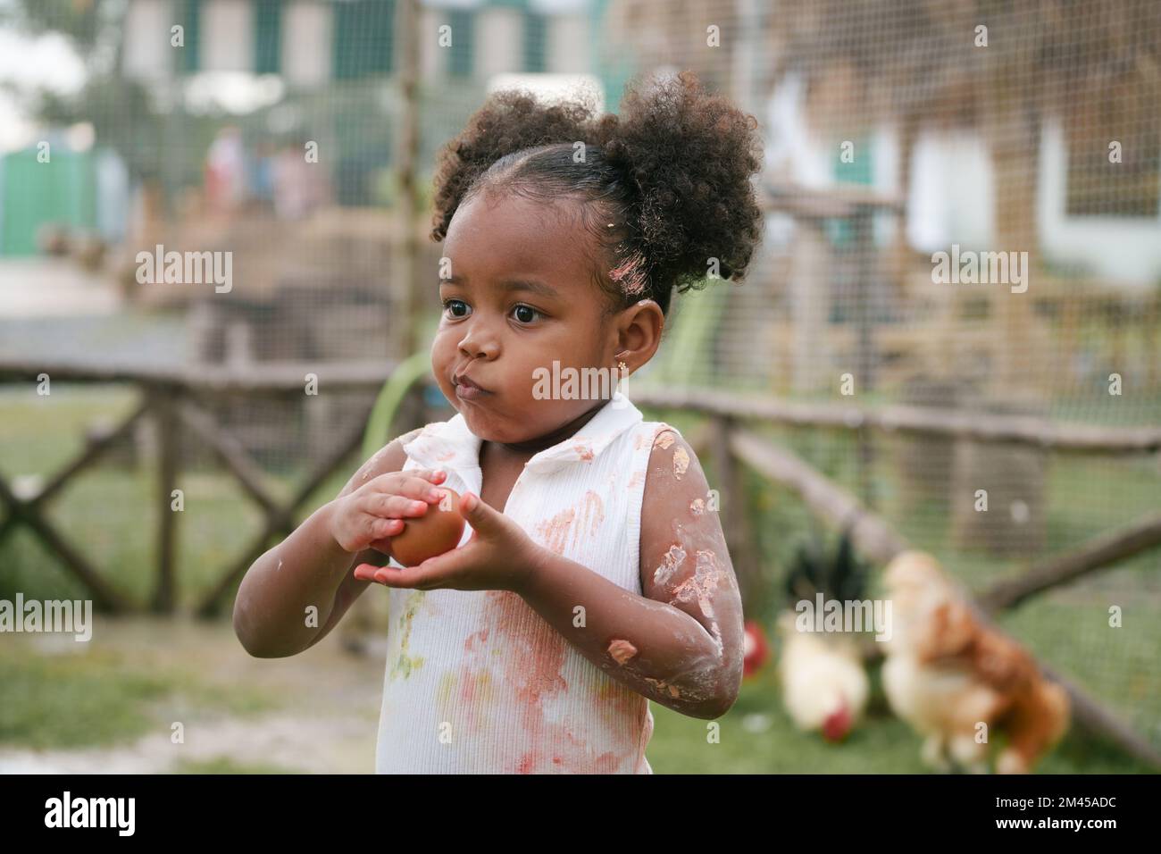 Enfant afro-américain tenant un œuf de poulet avec une coloration de couleur sur la main et la robe. Banque D'Images