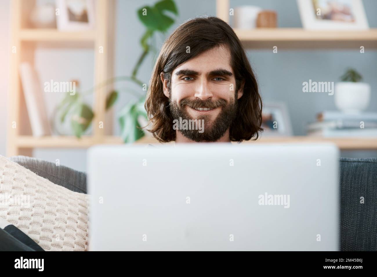 La connexion Internet est super et donne le sourire à tous. un beau jeune homme utilisant son ordinateur portable tout en se relaxant sur un canapé dans son salon. Banque D'Images