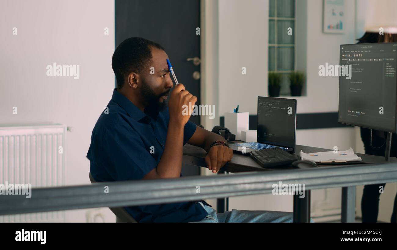 Un programme afro-américain pensif travaillant sur le développement de code et des idées de brainstorming pour créer un script html. Développeur de logiciels pensant au serveur de base de données dans le bureau de l'agence informatique. Banque D'Images