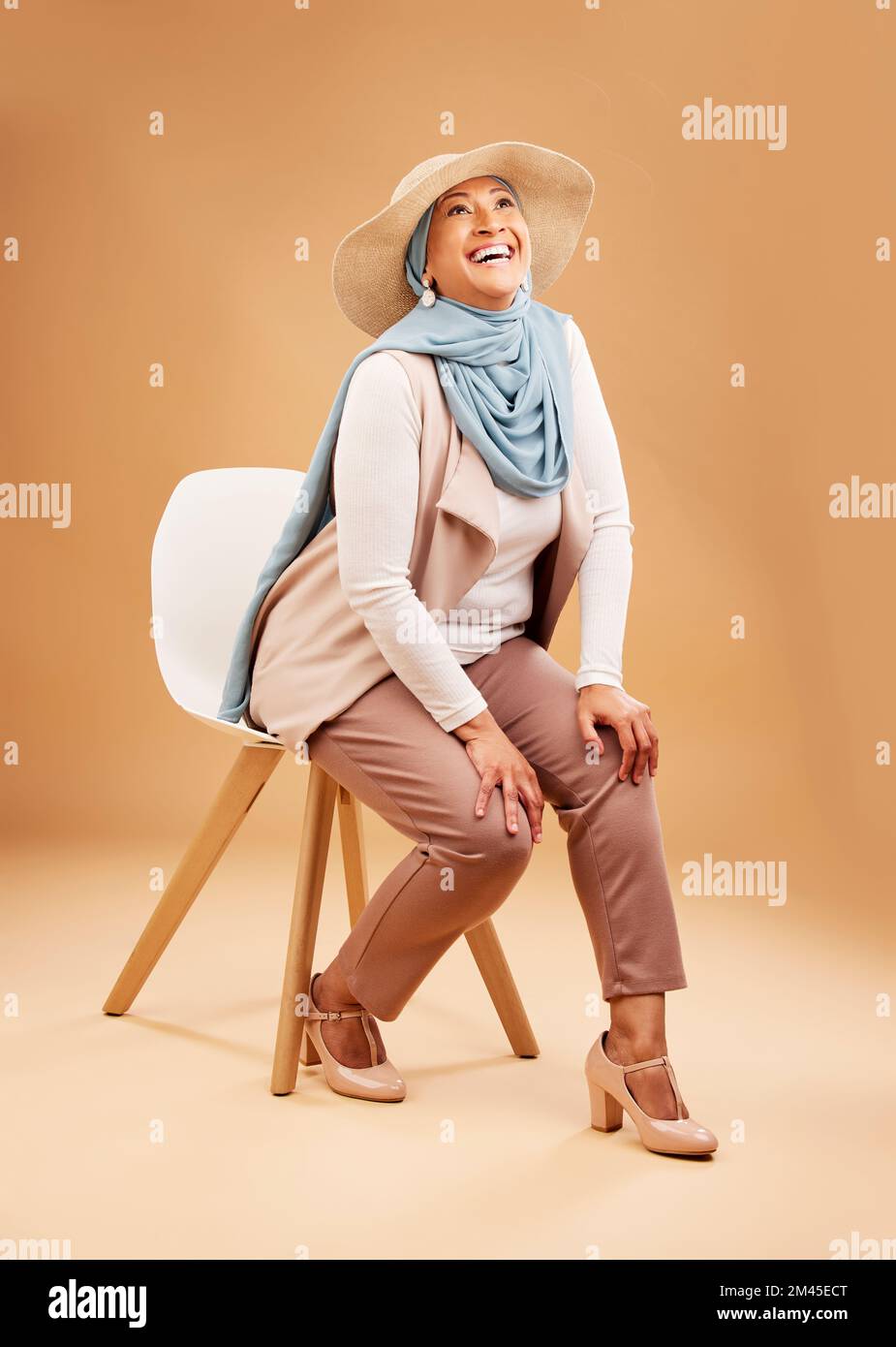 Femme musulmane, foulard de mode ou chaise en studio à Dubaï, chapeaux élégants et tendance ou vêtements arabes frais. Sourire heureux, rire ou mûrir Banque D'Images