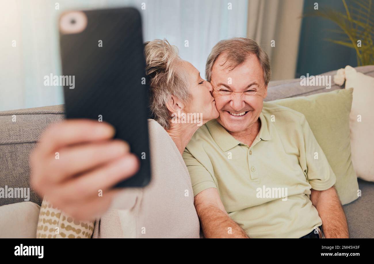 Senior, baiser et téléphone selfie d'un couple avec amour, soin et bonheur sur un canapé de salon. Heureux, sourire et mariage d'une femme et d'un homme ensemble Banque D'Images