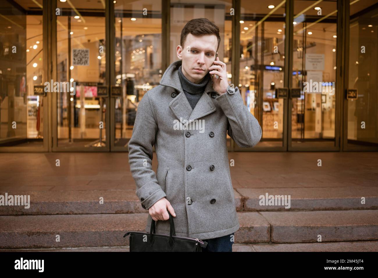Homme en manteau gris et chandail se tient sur la rue de ville. Parle au  téléphone. Résout les problèmes et les problèmes liés à l'entreprise et au  travail Photo Stock - Alamy