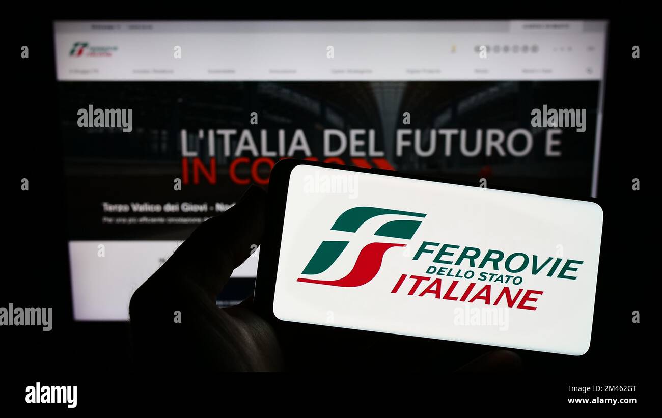Personne tenant un smartphone avec le logo de la société Ferrovie dello Stato Italiane S.p.A. à l'écran en face du site Web. Mise au point sur l'affichage du téléphone. Banque D'Images