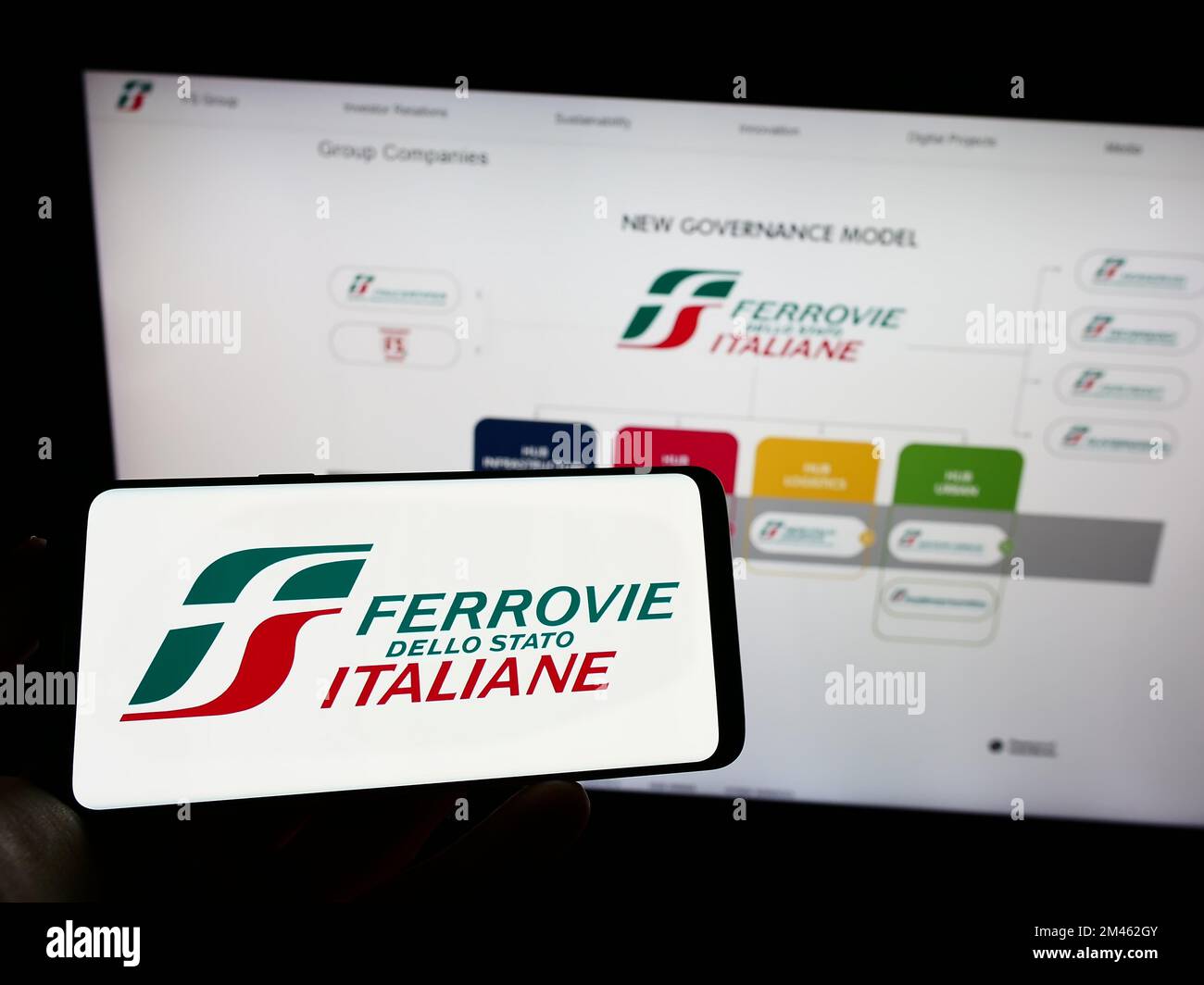 Personne tenant un téléphone portable avec le logo de la société Ferrovie dello Stato Italiane S.p.A. à l'écran en face de la page web. Mise au point sur l'affichage du téléphone. Banque D'Images
