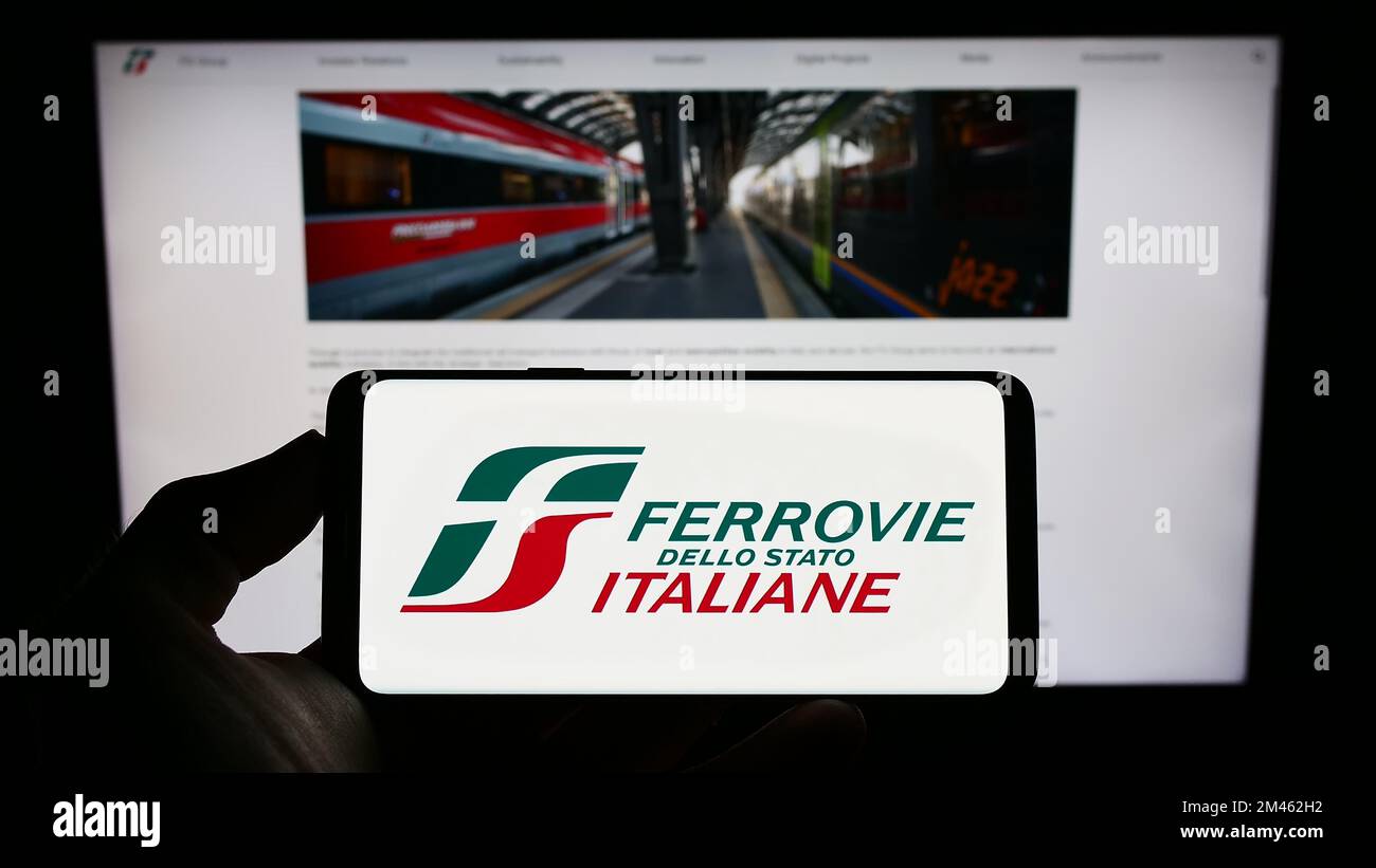 Personne tenant un téléphone portable avec le logo de la société Ferrovie dello Stato Italiane spa à l'écran en face de la page web d'affaires. Mise au point sur l'affichage du téléphone. Banque D'Images