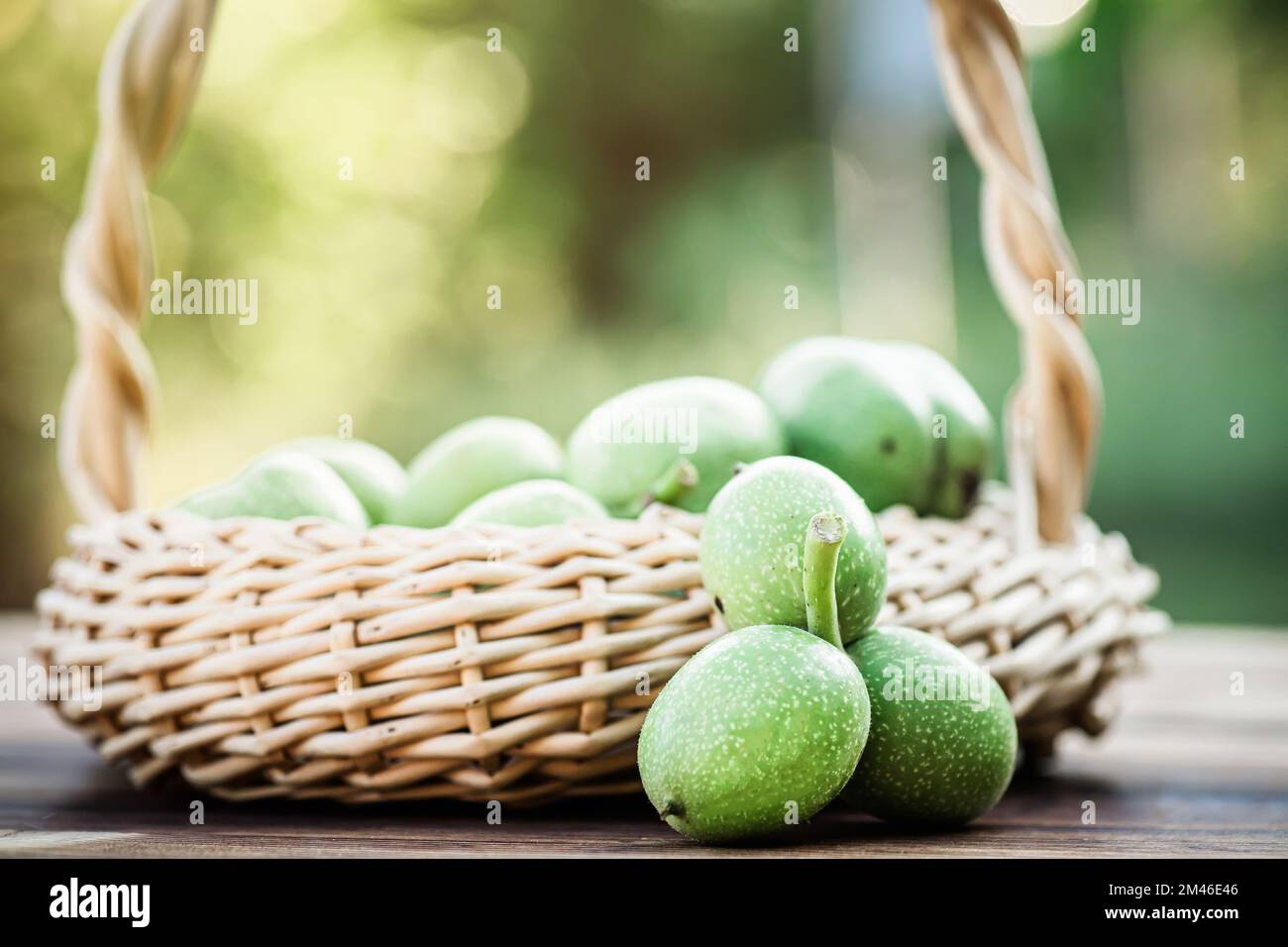 Noix vertes dans un panier en osier. Collection d'ingrédients pour des aliments sains. Ancienne table vintage et fruits de noyer entiers non mûrs. Banque D'Images