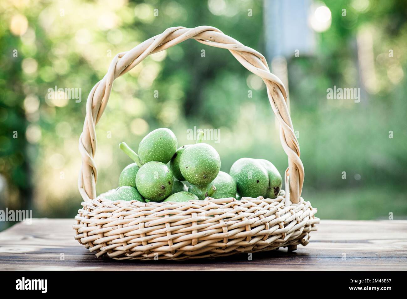 Noix vertes dans un panier en osier. Collection d'ingrédients pour des aliments sains. Ancienne table vintage et fruits de noyer entiers non mûrs. Banque D'Images