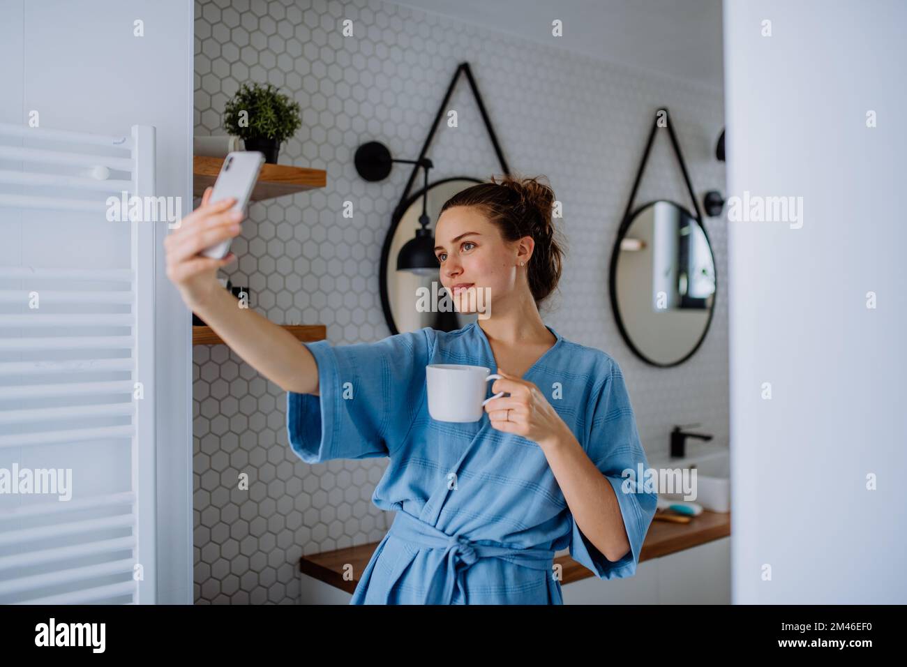 Jeune femme prenant le selfie dans la salle de bains, appréciant une tasse de café. Banque D'Images