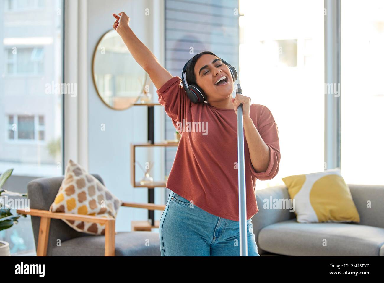 Musique, écouteurs et femme chantant tout en nettoyant la maison, dansant et s'amuser. Chanteur, danse et nettoyage de printemps féminin pour l'hygiène tenant le balai Banque D'Images