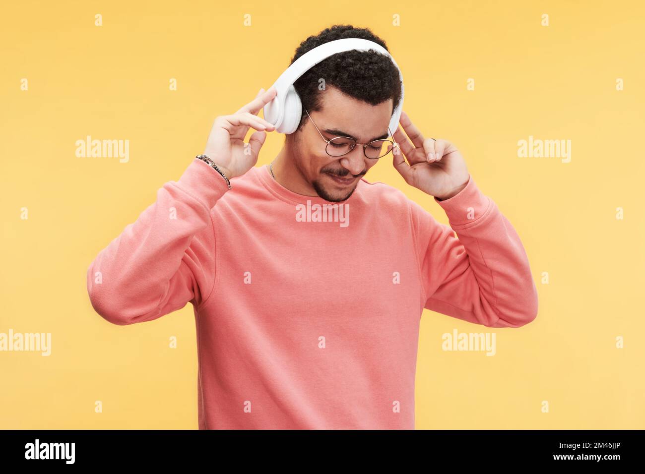 Un homme heureux en vêtements décontractés et lunettes qui garde les yeux fermés tout en appréciant sa musique préférée dans un casque sur fond jaune Banque D'Images