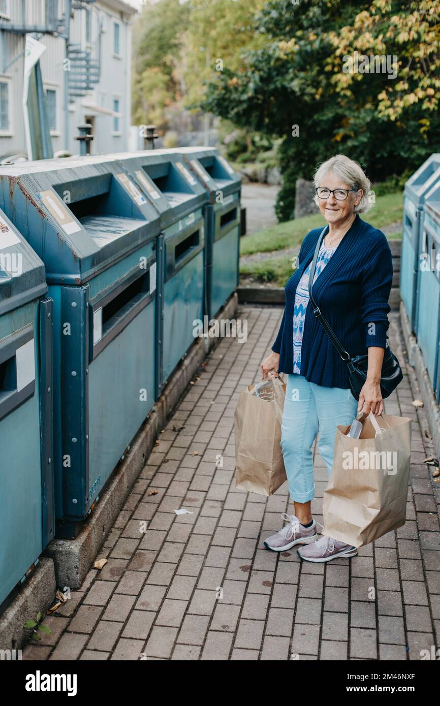 Femme avec des sacs en papier dans les bacs de recyclage Banque D'Images