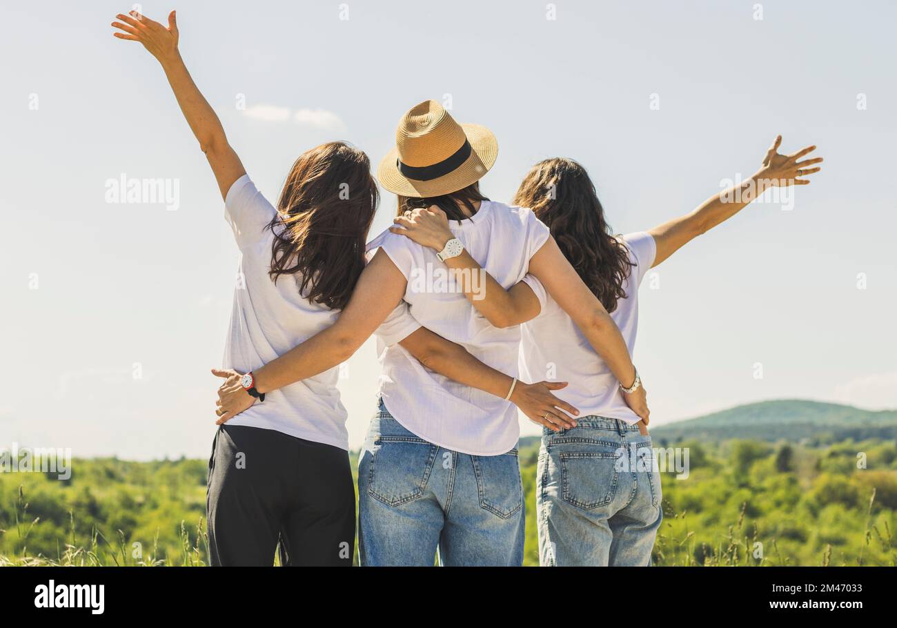 Vue arrière trois femmes s'embrassant et saluant la nature avec les mains vers le haut. Banque D'Images