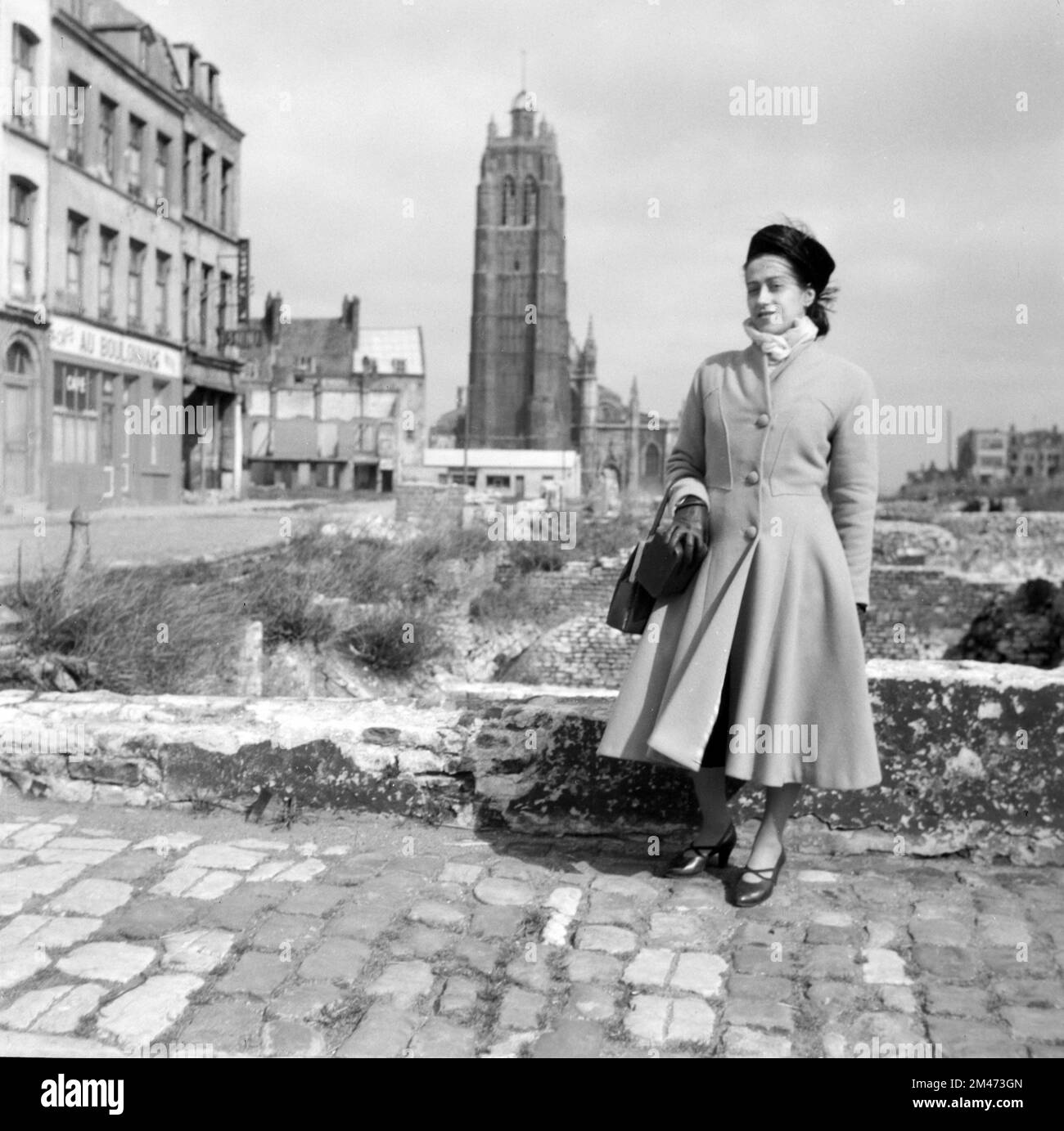 Femme française portant des vêtements de style 1940s ou de mode y compris le manteau plissé serré Dunkerque France 1949. En arrière-plan se trouve le beffroi sur pied avec un premier plan ruiné ou vacant, à la suite de dommages de guerre ou de bombardements pendant la Seconde Guerre mondiale, avant la reconstruction de Dunkerque après la guerre. Banque D'Images