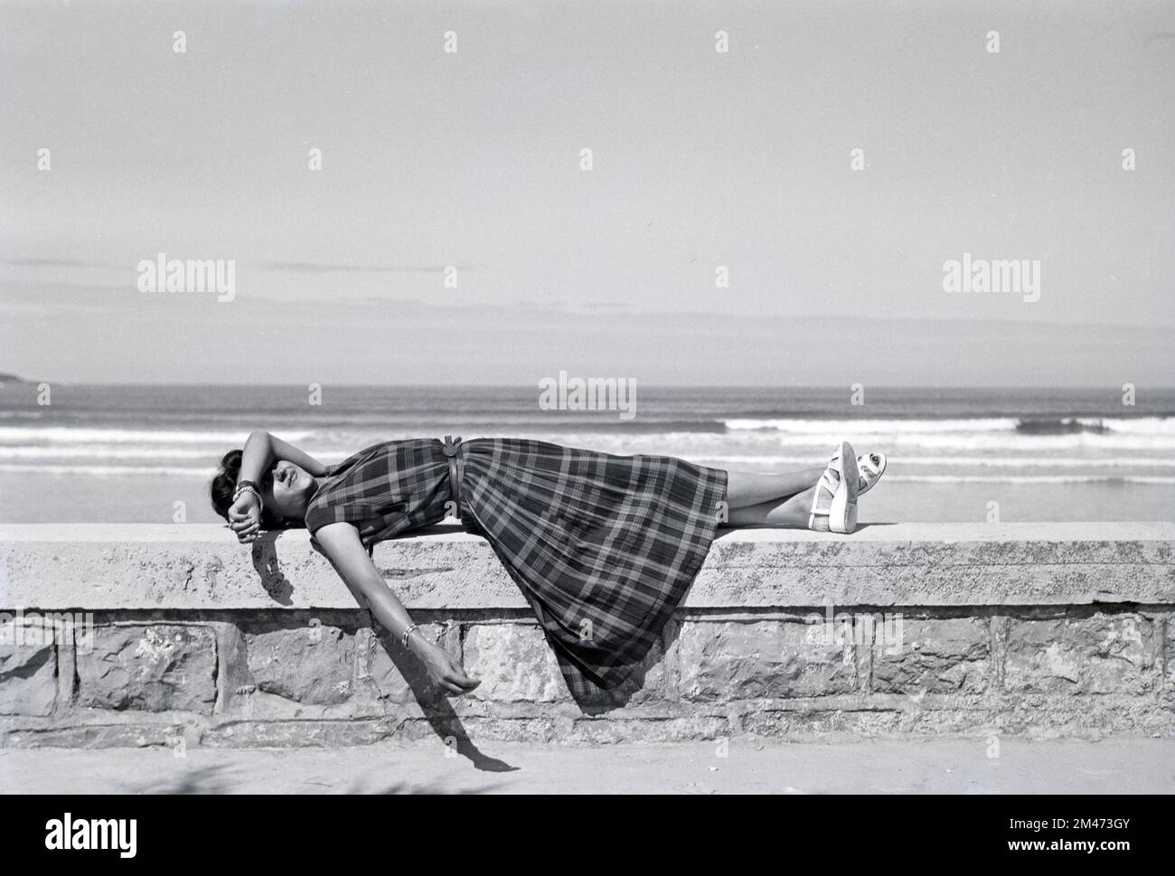 Jeune française ou 1950s femme portant un Tartan, un motif à carreaux, une robe à carreaux ou à carreaux recrée ou se détend sur le Seawall à Hendaye Pyrénées-Atlantiques France 1950 Banque D'Images