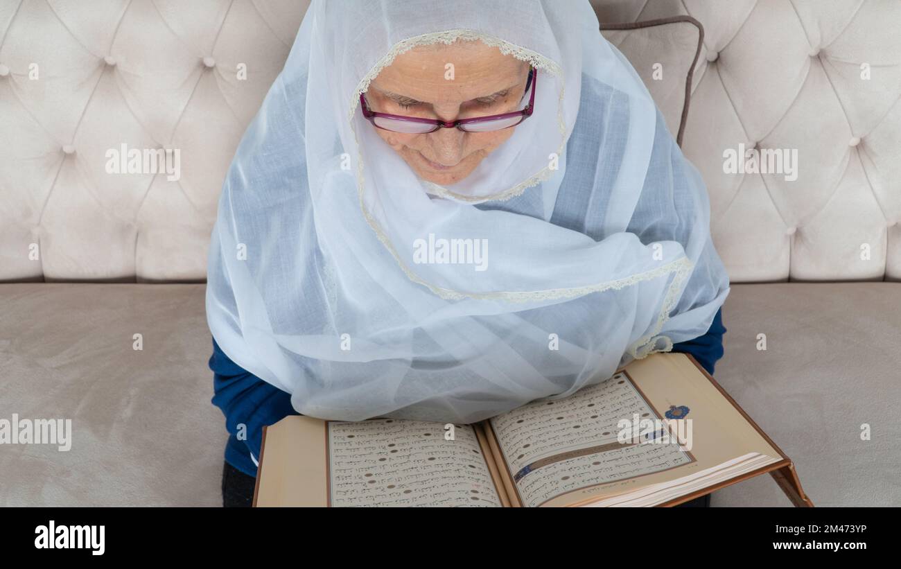 Vieille femme musulmane lisant le Saint Coran à la maison pendant le mois du Ramadan. Vieille femme portant le hijab blanc lisant le Coran Banque D'Images