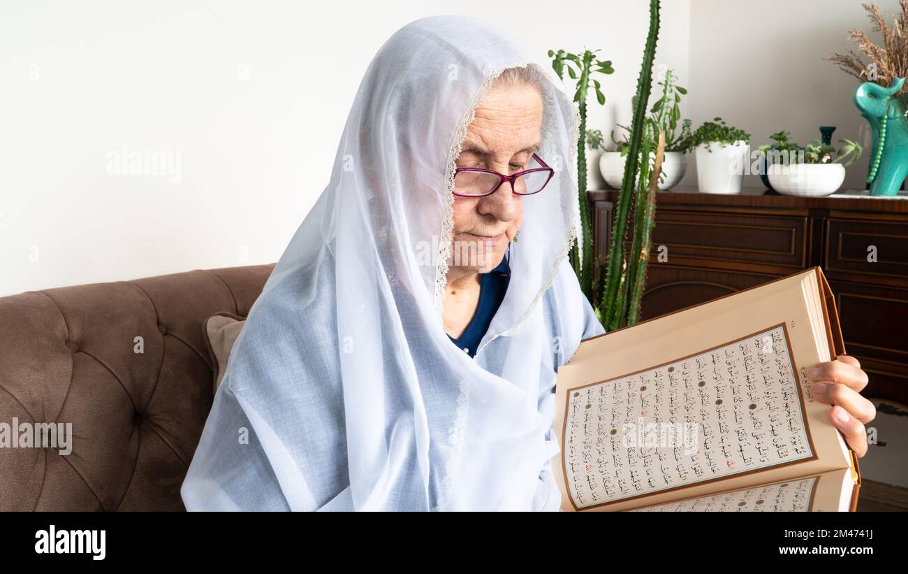 Vieille femme musulmane lisant le Saint Coran à la maison pendant le mois du Ramadan. Vieille femme portant le hijab blanc lisant le Coran Banque D'Images