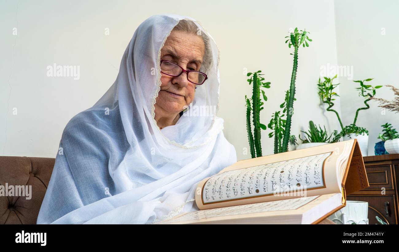 Vieille femme musulmane lisant le Saint Coran à la maison pendant le mois du Ramadan. Vieille femme portant le hijab blanc lisant le Coran Banque D'Images