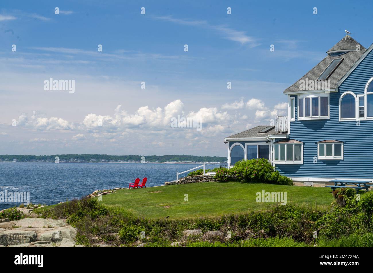 Vue sur une Maison bleue au bord de la mer avec deux chaises rouges, phare de Nubble, Maine, Etats-Unis Banque D'Images