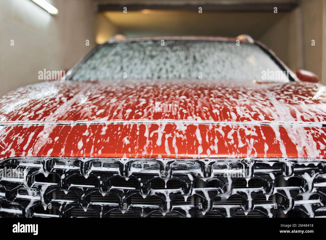 Voiture sport rouge moderne de luxe recouverte de mousse. Lavage de voiture. Photo en gros plan du capot de voiture dans le service de lavage de voiture intérieur. Banque D'Images