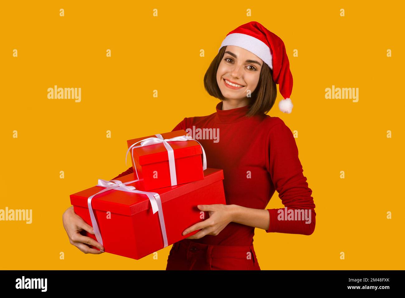 Joyeuse jeune femme brune en chapeau de père Noël tenant des cadeaux de Noël Banque D'Images