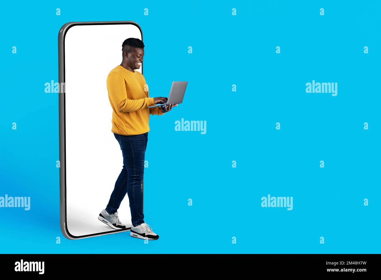 Black Young Man utilisant un ordinateur portable tout en sortant du grand écran de smartphone Banque D'Images