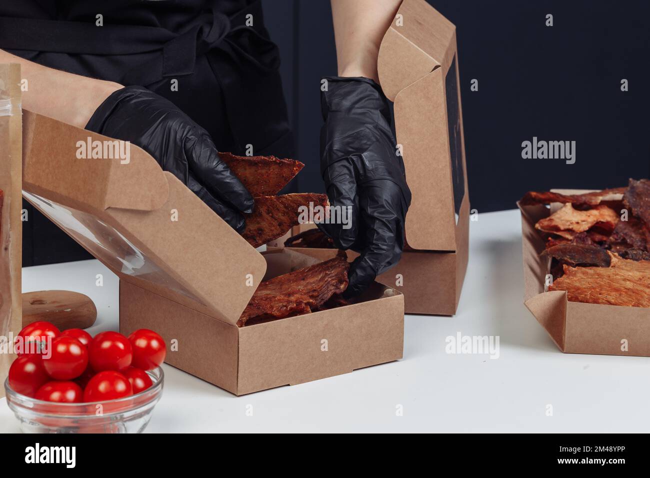 un gars met de la viande séchée dans des boîtes en papier dans des gants noirs. Photo de haute qualité Banque D'Images