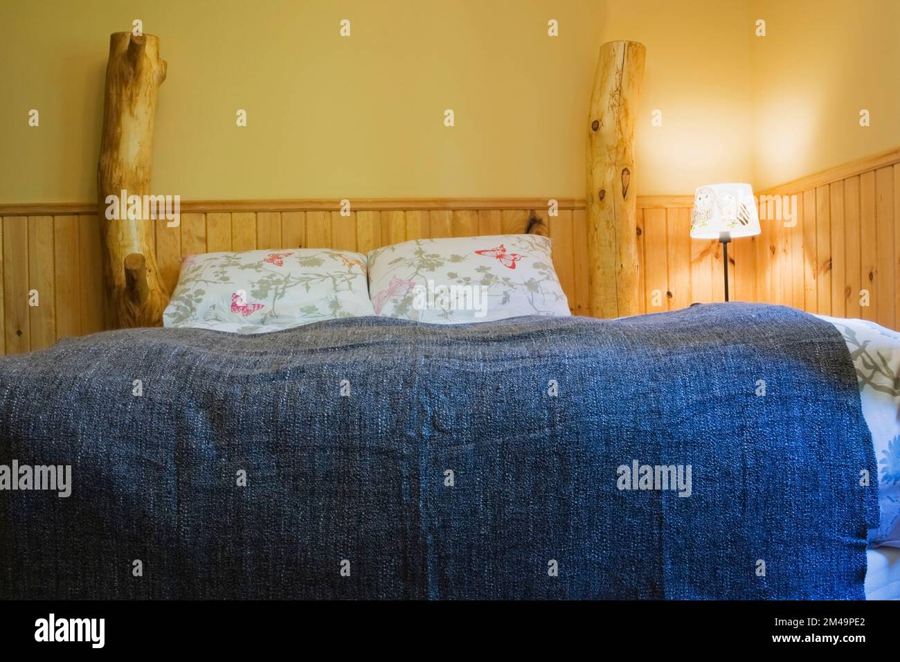 Lit rustique à baldaquin recouvert d'un couvre-lit en denim bleu dans la chambre à l'étage à l'intérieur de la maison en rondins. Banque D'Images