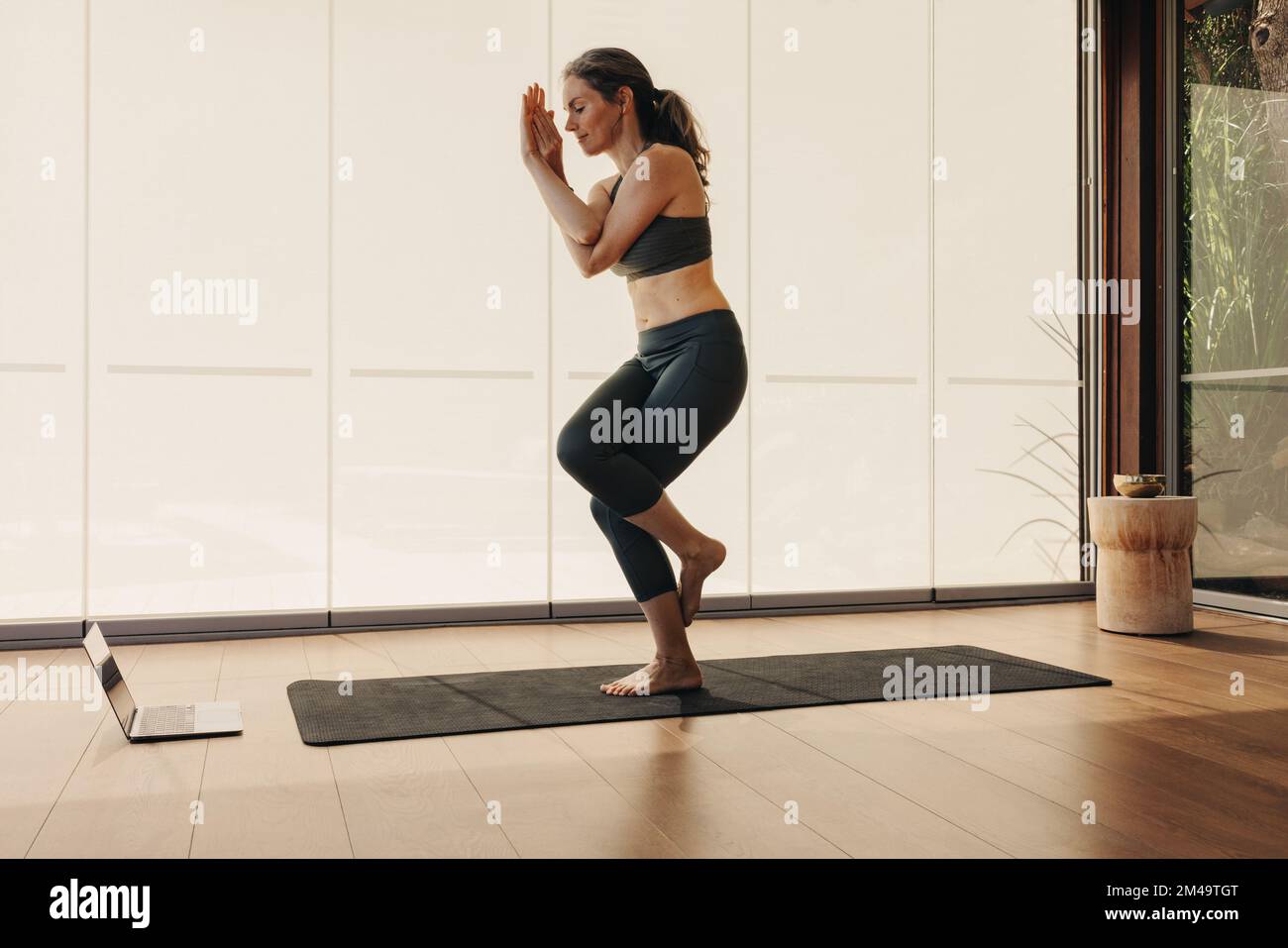 Femme âgée qui pose une jambe pendant un cours de yoga en ligne à la maison. Femme mature pratiquant un asana d'équilibre sur un tapis de yoga. La femme suit Banque D'Images