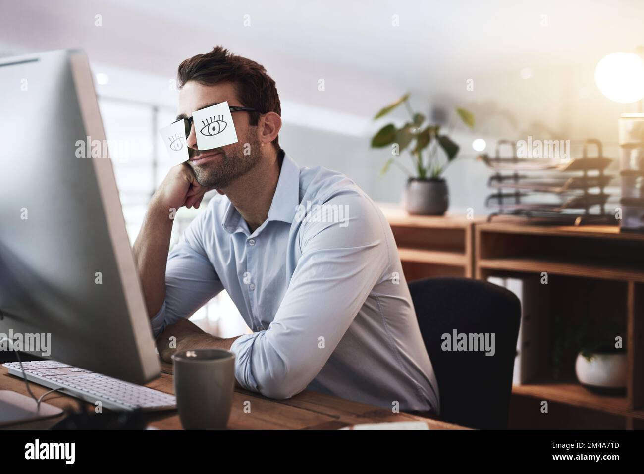 Ne pas déranger. un jeune homme d'affaires travaillant tard dans un bureau avec des notes adhésives couvrant ses yeux. Banque D'Images