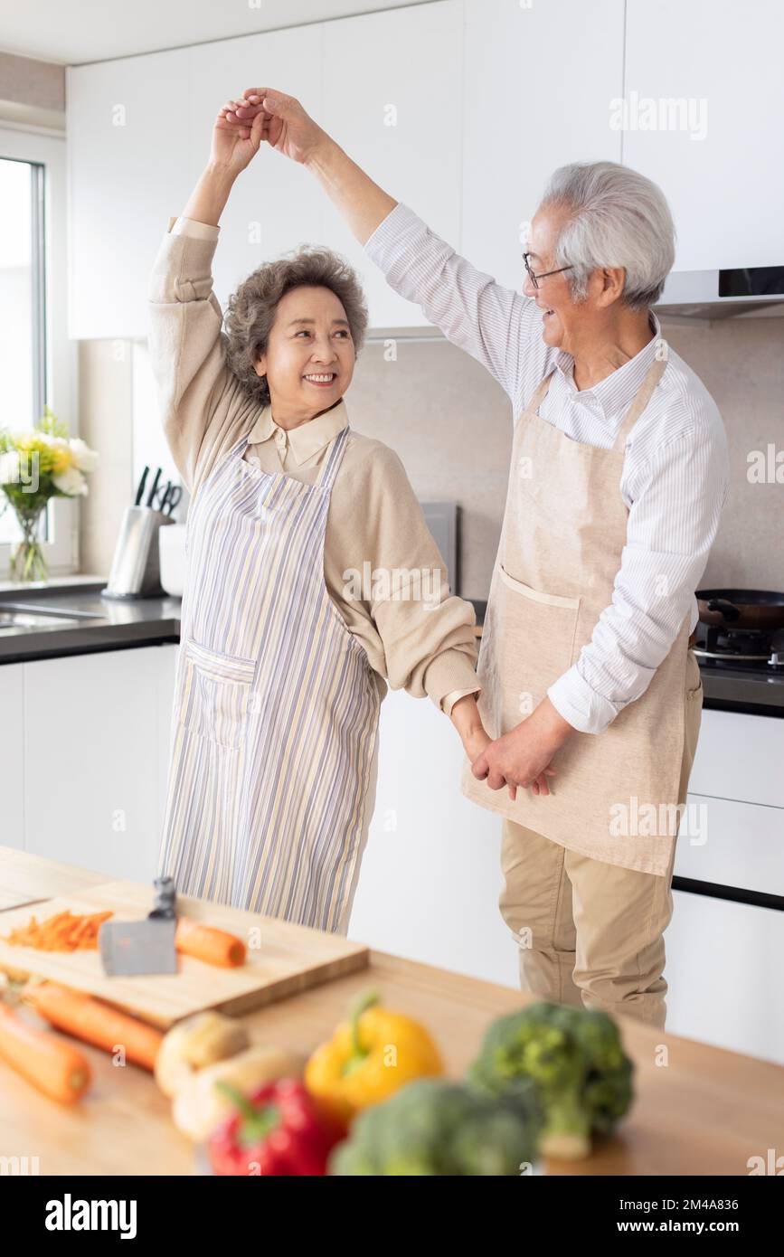 Couple chinois senior joyeux dansant dans la cuisine Banque D'Images