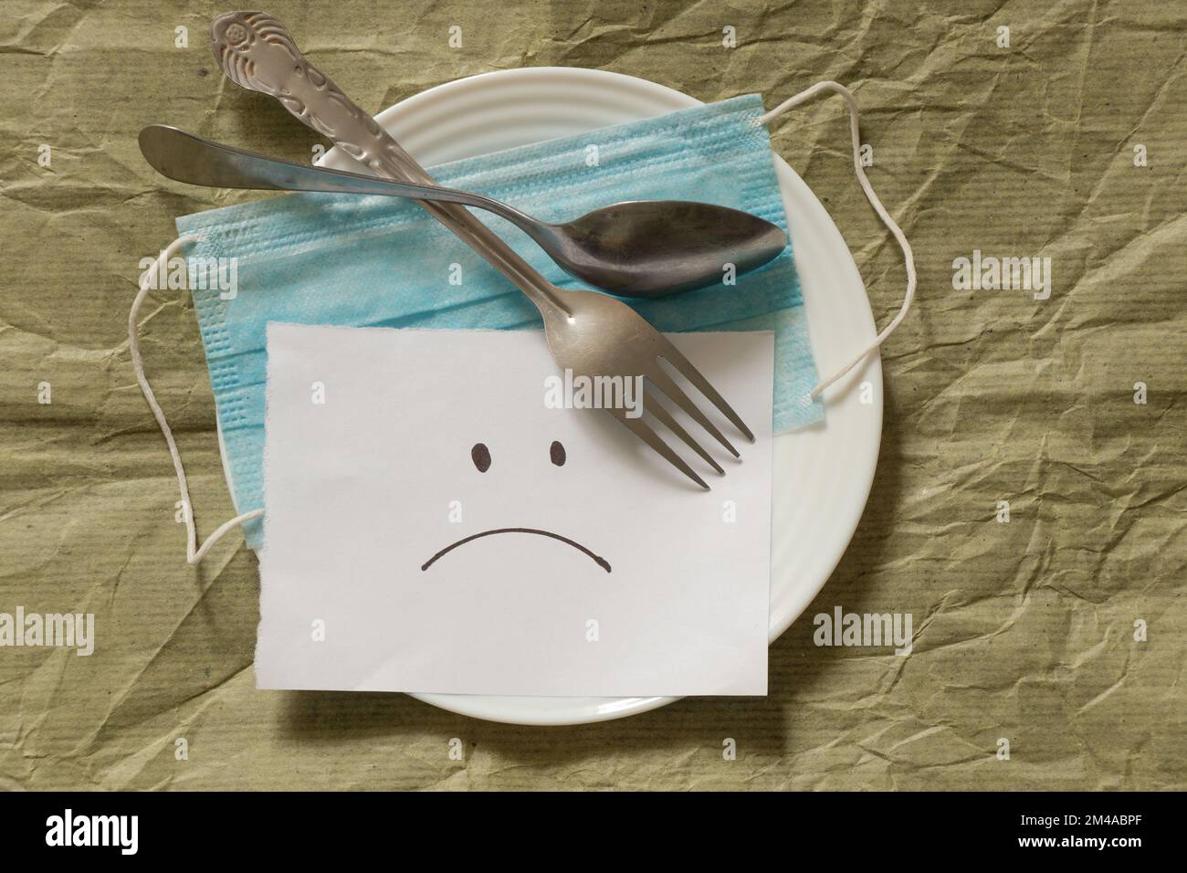 Masque médical un smiley triste est dessiné sur papier blanc sur fond vert dans une assiette avec Banque D'Images