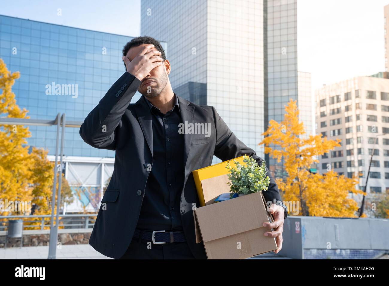Homme d'affaires avec boîte en carton avec fournitures de bureau debout à l'extérieur du bâtiment de bureau. Concept déclenché Banque D'Images