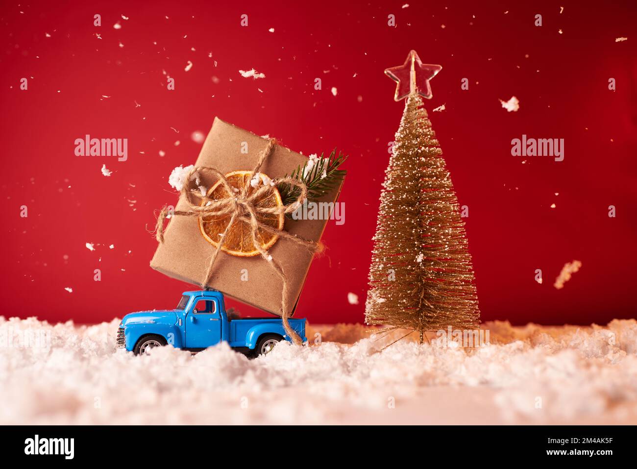 Une voiture-jouet porte un grand cadeau pour le nouvel an et Noël sur fond rouge Banque D'Images