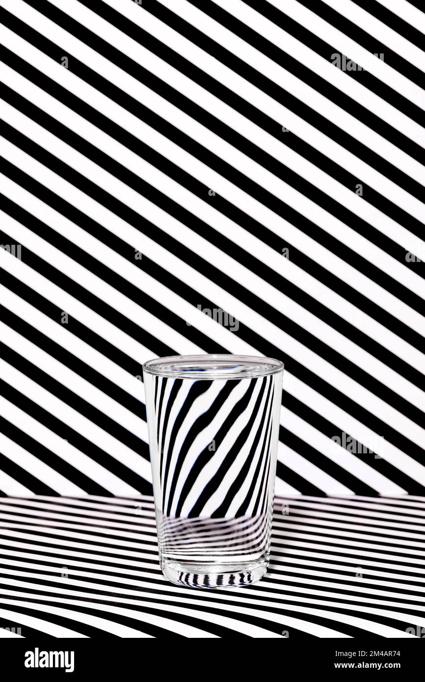 Verre transparent d'eau placé dans un studio rayé noir et blanc avec illusion optique Banque D'Images