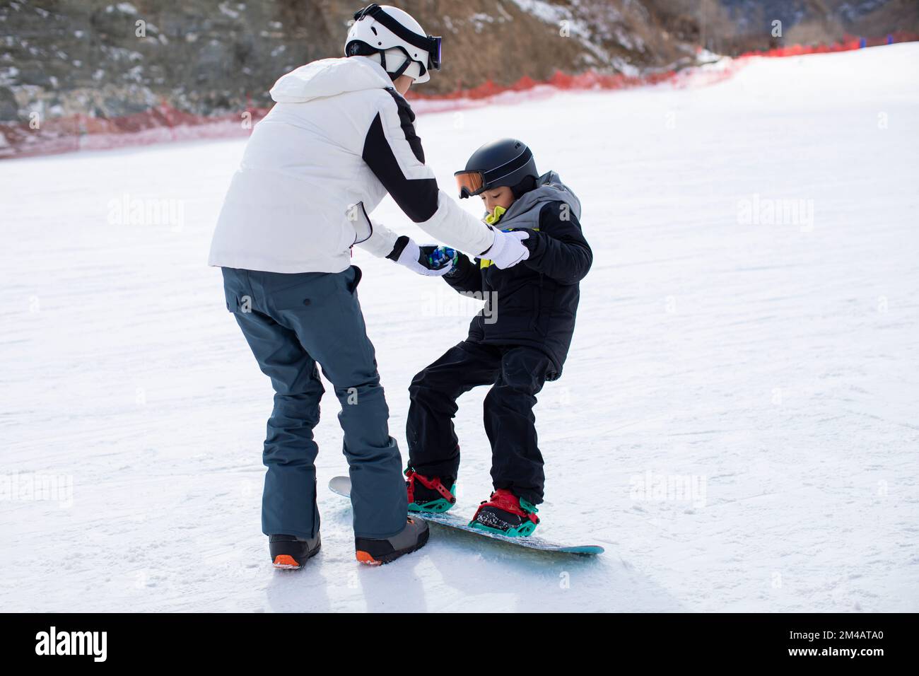 Petit garçon chinois apprenant à faire du snowboard avec son entraîneur Banque D'Images
