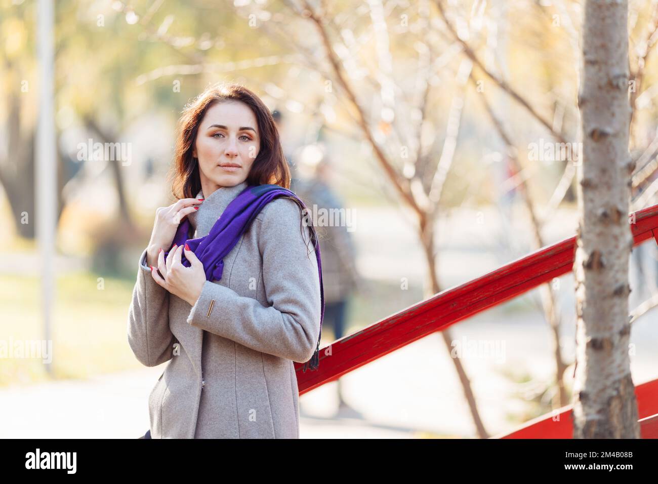 portrait d'une jeune femme avec de longs cheveux respirent de l'air frais un jour ensoleillé d'automne et portant un manteau gris et une écharpe violette. Photo de haute qualité Banque D'Images
