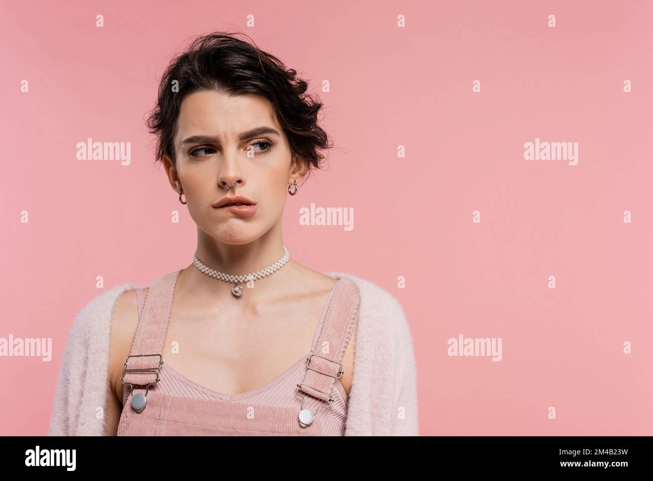 femme offended dans collier de perles mordant lèvre et regardant loin isolé sur rose Banque D'Images